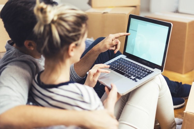 A couple sits on a couch and investigates buying a new home