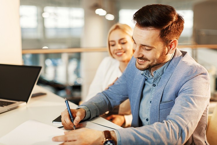 A man's partner looks on as he signs a mortgage