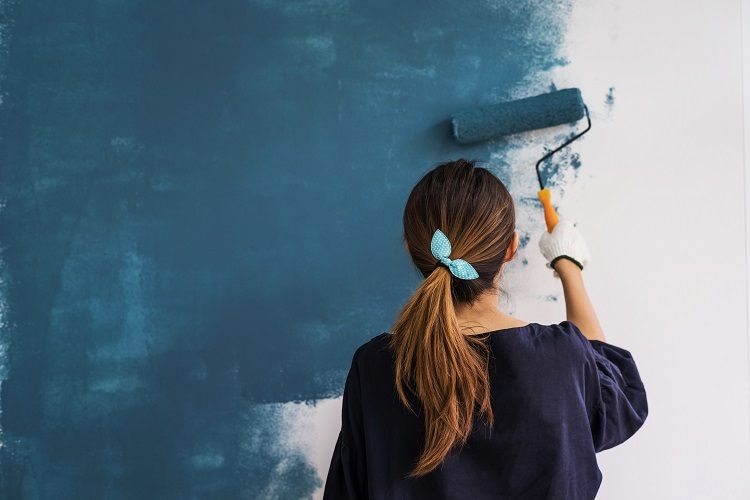 A young woman paints a wall in her home to raise the value