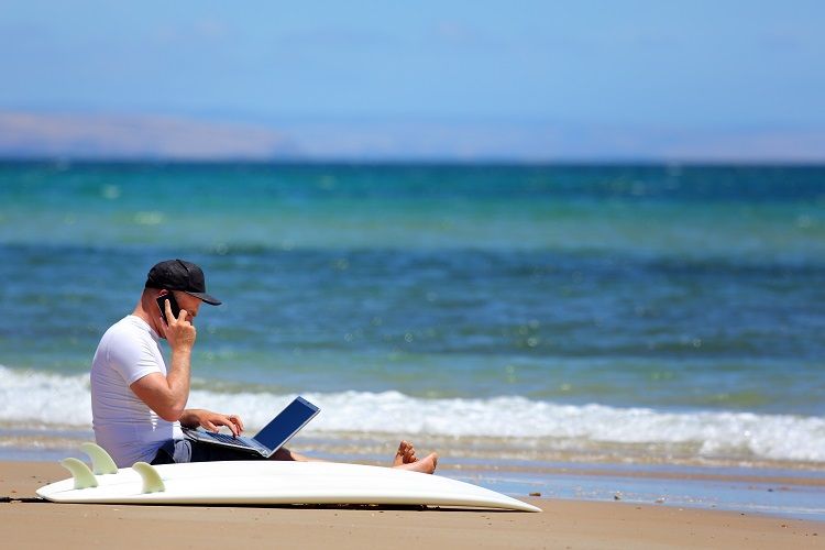 A casual worker applies for a mortgage sitting on the beach next to a surfboard