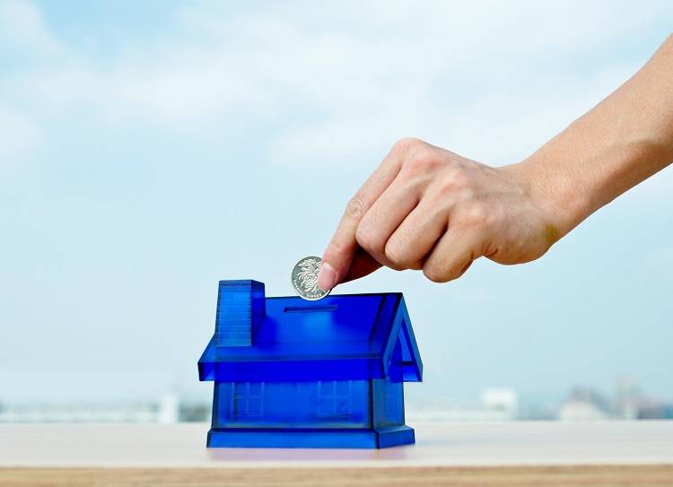 A man puts a coin in a plastic house representing an investment property